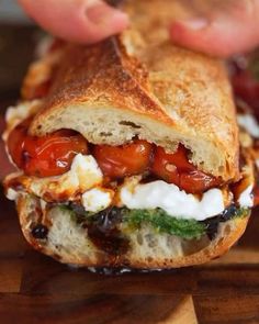 a sandwich with tomatoes, mozzarella and other toppings is being held by someone