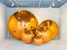 several shiny gold balls sitting in a room with white walls and ceiling lights above them