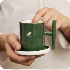 a person holding a green coffee cup with a flower painted on it