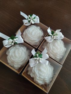 four cupcakes with white frosting and bows in small boxes on a table