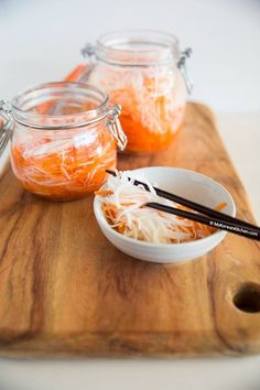 two jars filled with food sitting on top of a wooden cutting board next to chopsticks