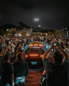 a group of people standing around a car at night with their cell phones in the air