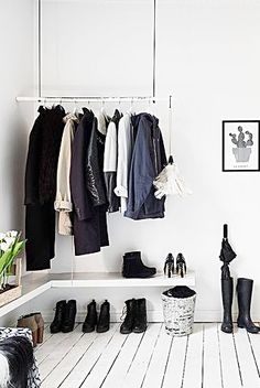 a white room with black and white clothes hanging on the wall, shoes are lined up in front of an open closet door