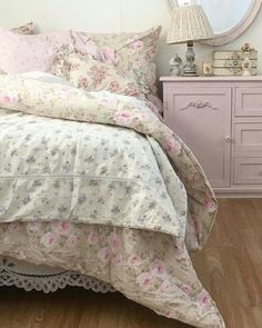 a white bed with pink and blue flowers on it in a bedroom next to a dresser