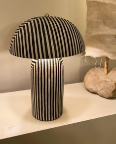 a black and white striped lamp sitting on top of a table next to a rock