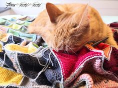 an orange cat laying on top of a pile of crocheted blankets