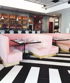 a restaurant with black and white checkered flooring, pink velvet booths and tables