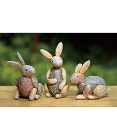 three small rabbits sitting next to each other on a wooden table with trees in the background