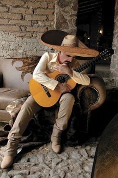 a man in a sombrero sitting on a couch with a guitar and hat