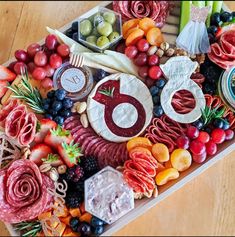 a platter filled with meats, cheeses and fruit on top of a wooden table