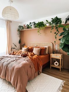 a bed with orange sheets and pillows in a bedroom next to a potted plant