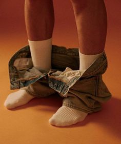 the legs and ankles of a person in jeans with white socks, standing on an orange background