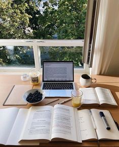 an open book sitting on top of a wooden table next to a laptop computer and cup of coffee