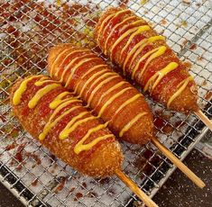 four hot dogs on sticks covered in ketchup and mustard sitting on a grill