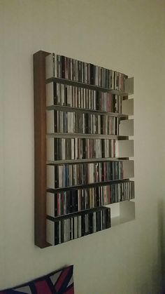 a wall mounted shelf filled with dvd's on top of a wall next to a bed