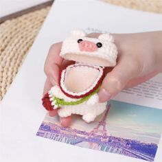 a hand holding a small crocheted animal in front of an open book with the eiffel tower in the background