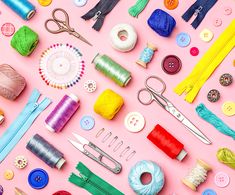 sewing supplies laid out on a pink surface with buttons, needles, and other items