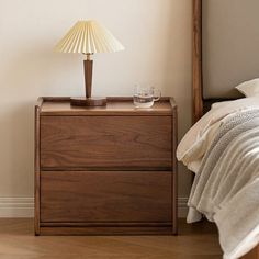 a nightstand with a lamp on it next to a bed