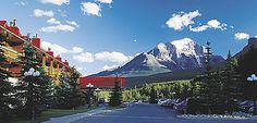 a street lined with tall buildings and mountains in the background, surrounded by pine trees