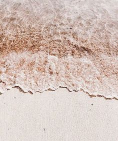 an ocean wave rolls in on the sand at the edge of the beach, as seen from above