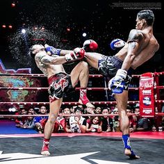 two men kick each other in the middle of a boxing ring