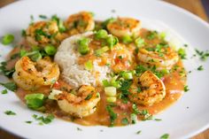 a white plate topped with shrimp and rice covered in gravy on top of a bed of green onions