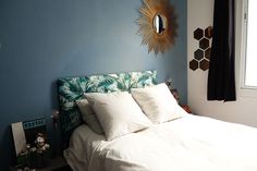 a bedroom with blue walls and white bedding, palm leaves on the headboard