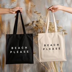 two people holding black and white bags with the words beach please on them next to dried plants