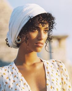 a woman with curly hair wearing a white head wrap and ear studs on her left ear