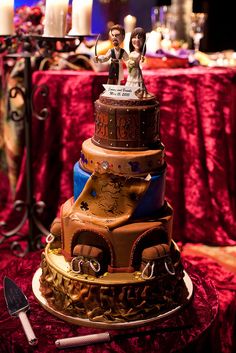 a three tiered cake is decorated with figurines on top and candles in the background