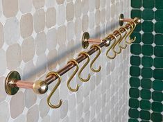 four brass hooks hang on the wall next to a green tiled wall with white tiles