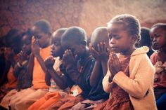 a group of young children sitting next to each other in front of a wall with their hands together