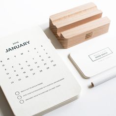 a desk with a calendar, pen and wooden block on it next to a notepad