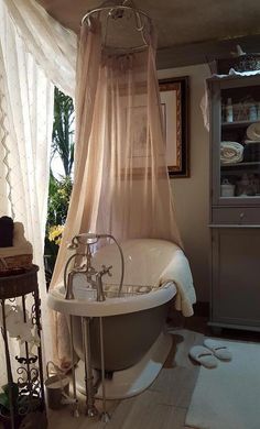 an old fashioned claw foot bathtub in the corner of a bathroom with sheer curtains