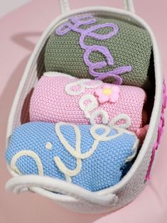 three knitted items are sitting in a small bag on a pink surface with the word love spelled out