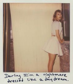 a woman in a short white dress standing next to a wall with writing on it