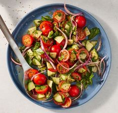 a blue plate topped with cucumber, tomatoes and onions next to a spoon