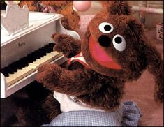 a teddy bear is playing the piano while someone holds it up to his ear and looks like he's smiling