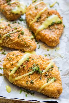 four pieces of breaded chicken covered in cheese and parsley on top of parchment paper