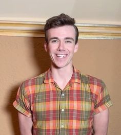 a man standing in front of a wall wearing a plaid shirt and smiling at the camera