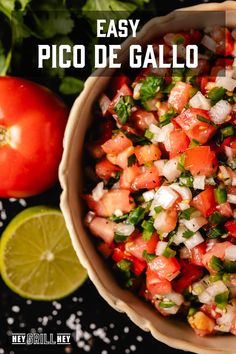 a bowl filled with salsa next to tomatoes and cilantro on a black surface