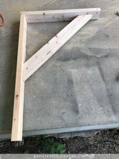 a wooden frame sitting on top of cement next to a pair of scissors and pliers