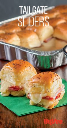 two sliders sitting on top of a green napkin next to a pan of food