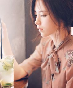 a woman sitting at a table with a drink in front of her and looking out the window