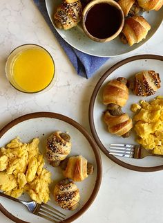 two plates with croissants and eggs on them next to a glass of orange juice