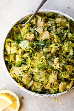 a bowl filled with broccoli and some lemon wedges next to a spoon