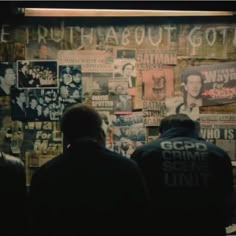 people standing in front of a wall covered with posters