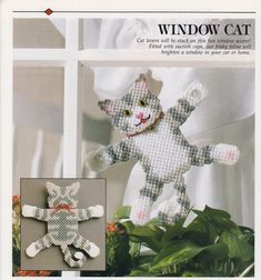 a cross stitch cat sitting on top of a potted plant next to a window