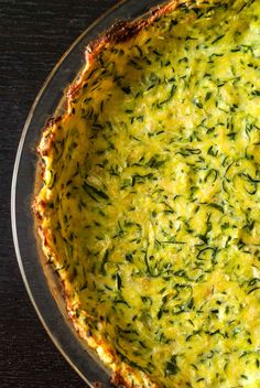 a quiche with cheese and spinach in a glass pie dish on a wooden table