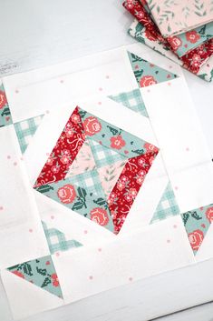 the block is laying on the table next to some scissors and sewing needles, which are also used for quilting